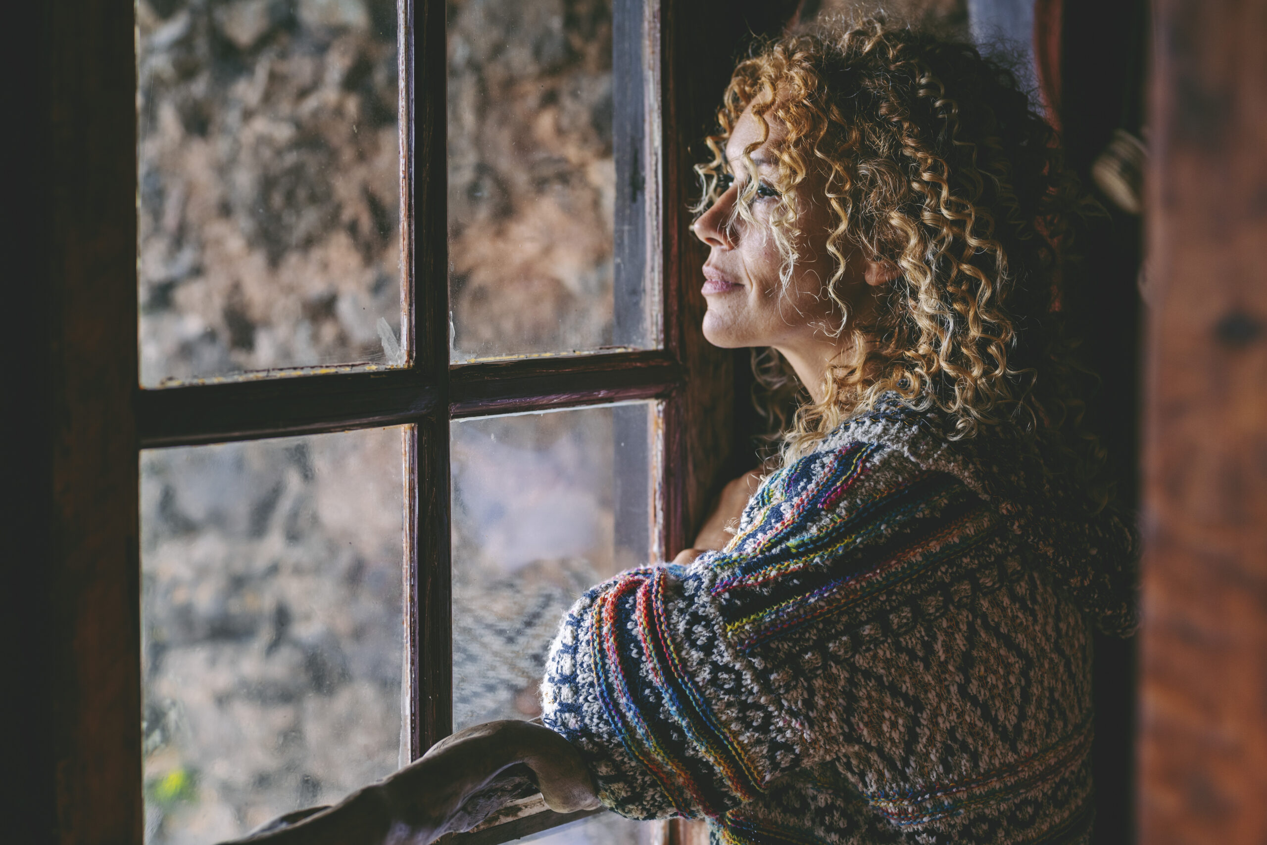 One alone woman standing at home near the window looking outside One alone woman standing at home near the window looking outside and thinking. Single female people lifestyle. Waiting friends and thoughts. Young lady indoor leisure. Side portrait of middle age